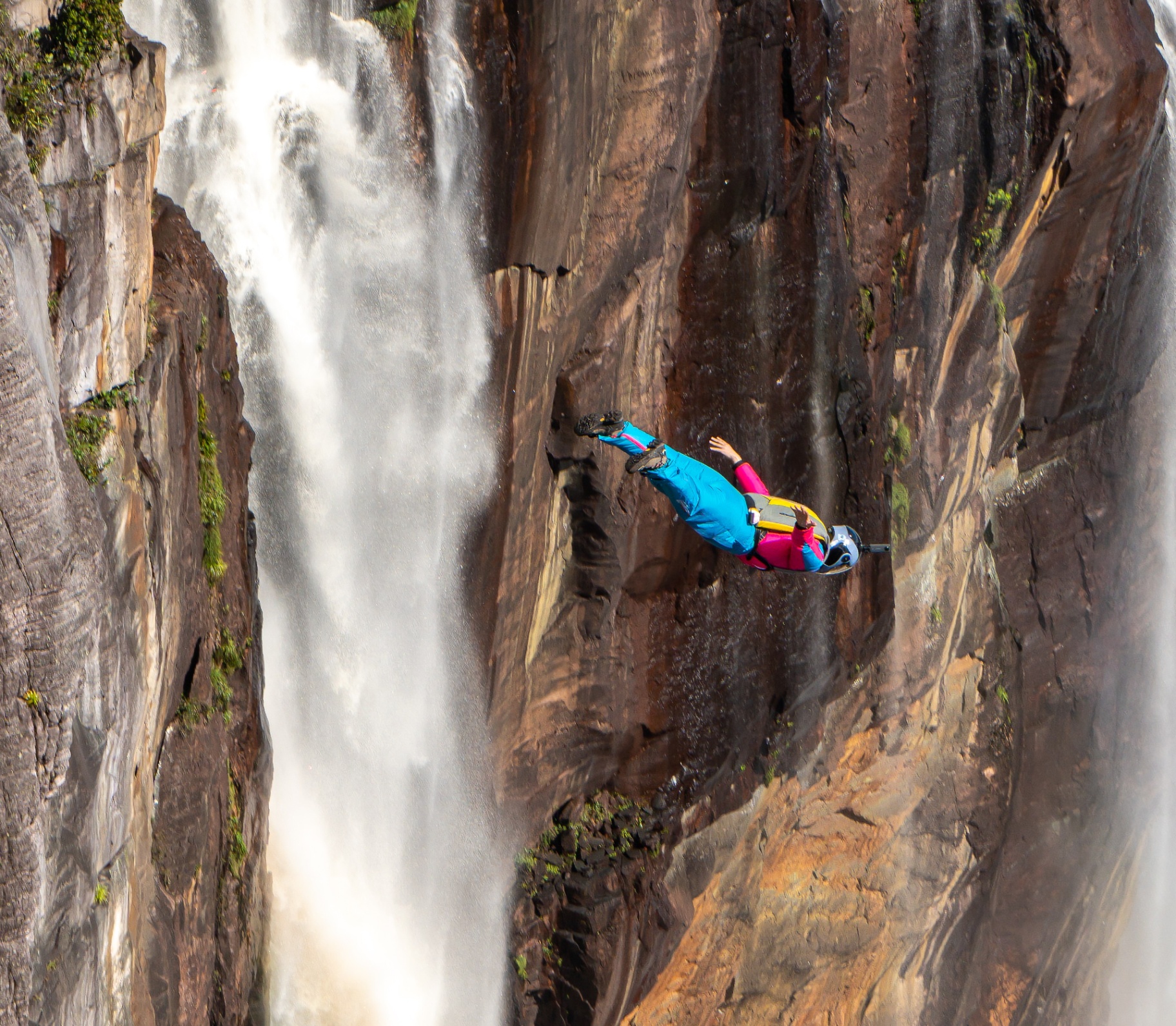 BASE jumper leaping from a cliff beside a waterfall