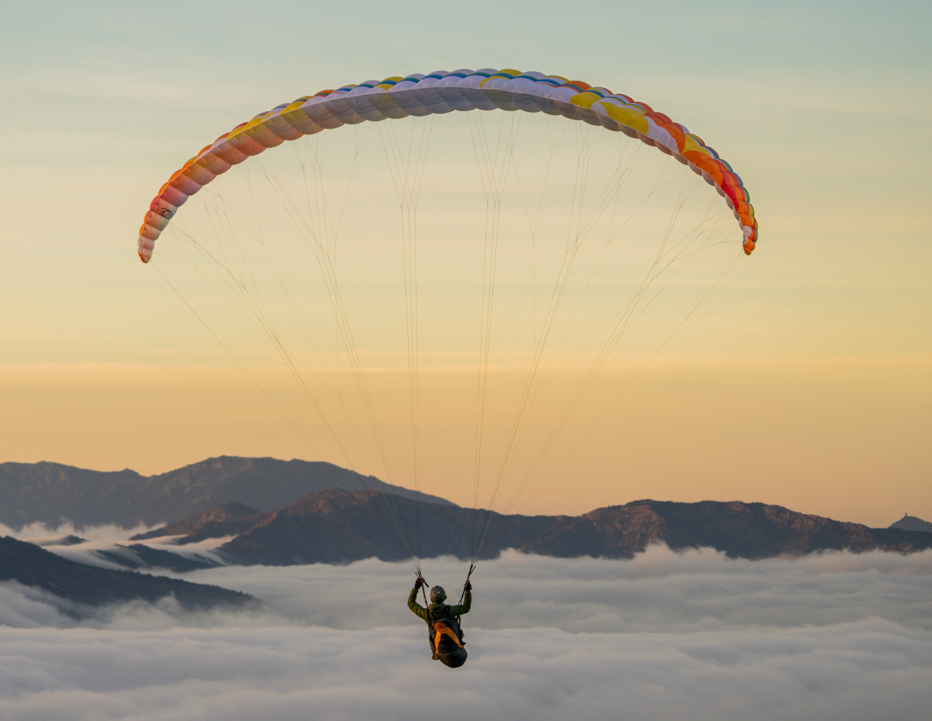 Paraglider flying over snowy mountain range at sunset