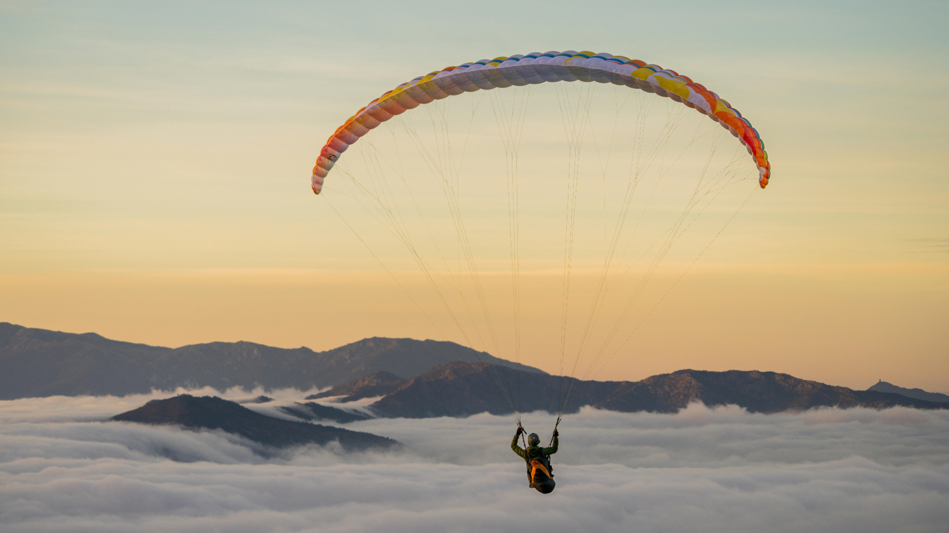 Paraglider soaring above a desert mountain range at golden hour